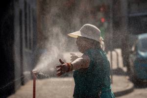 Person in sun hat stands in front of misting station to cool off